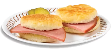 Two City Ham Biscuits at Waffle House with wet cured city ham on buttermilk biscuits served on white plate with side of grits